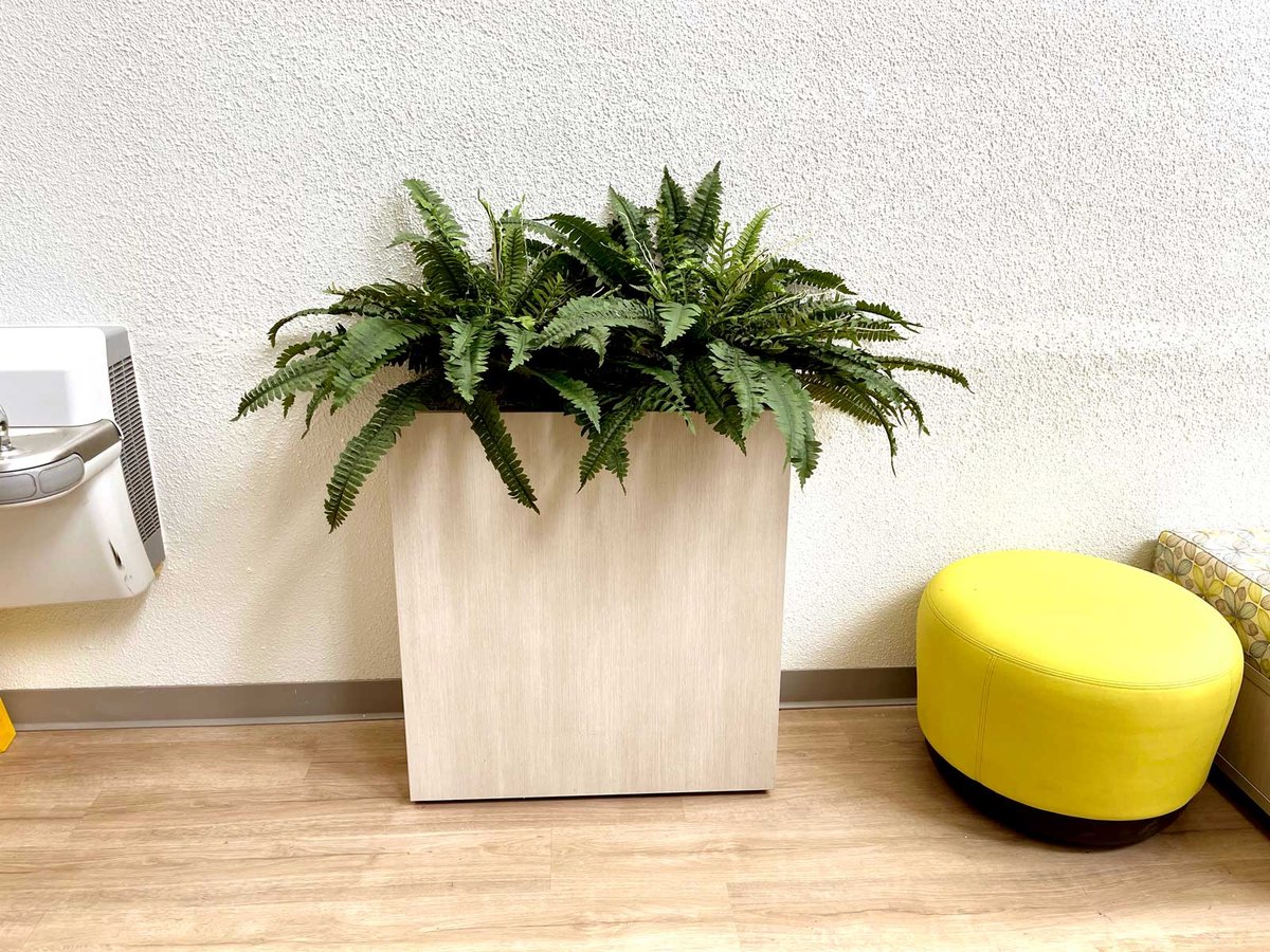 A wooden plant holder with a replica plant and a yellow ottoman 