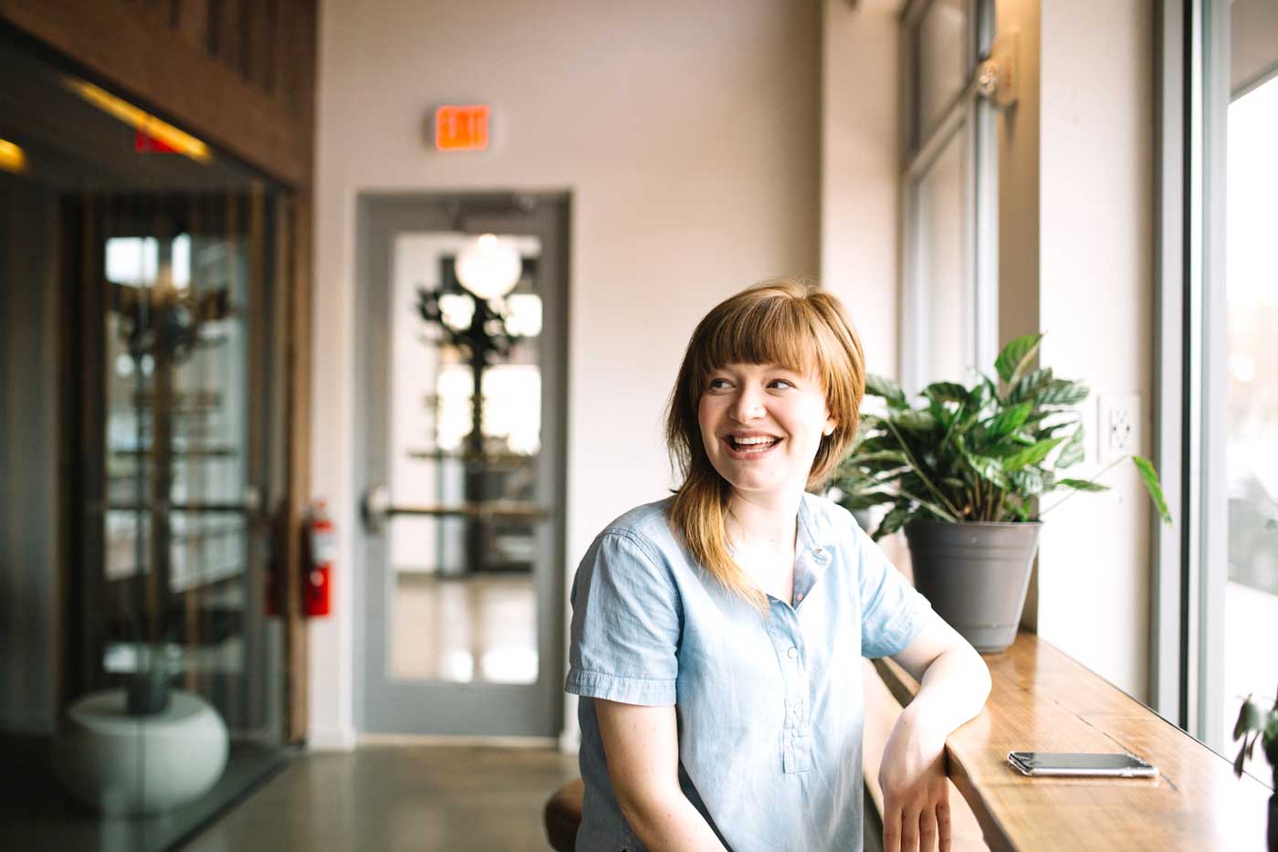 A woman sitting at a table and on the table is a plant and a phone 